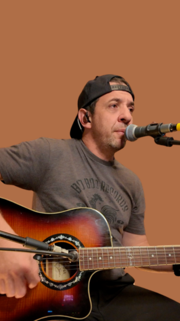 Sean Eddy press photo: country, blues, and rock singer playing a sunburst acoustic guitar on a warm brown background