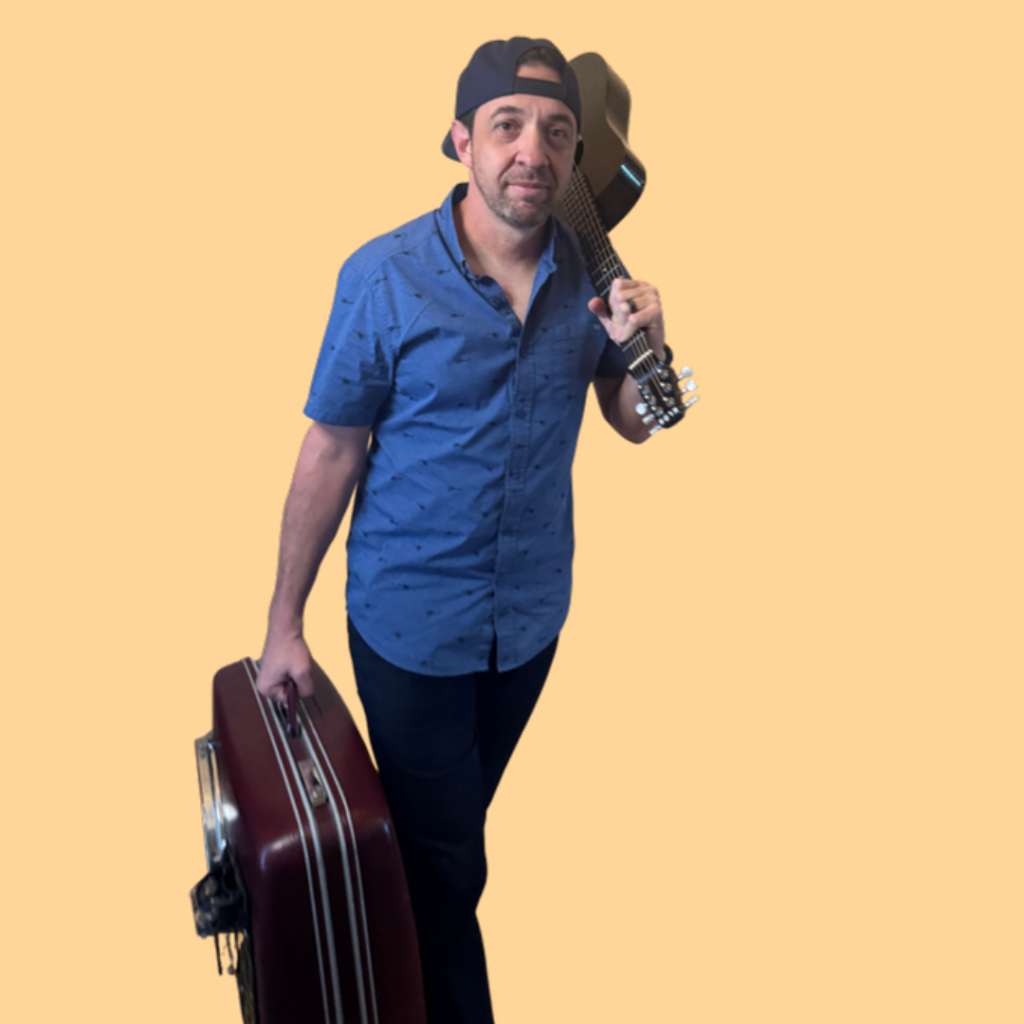 Sean Eddy, live looping musician from DFW, walking with a guitar over his shoulder and a vintage suitcase drum on a peach background